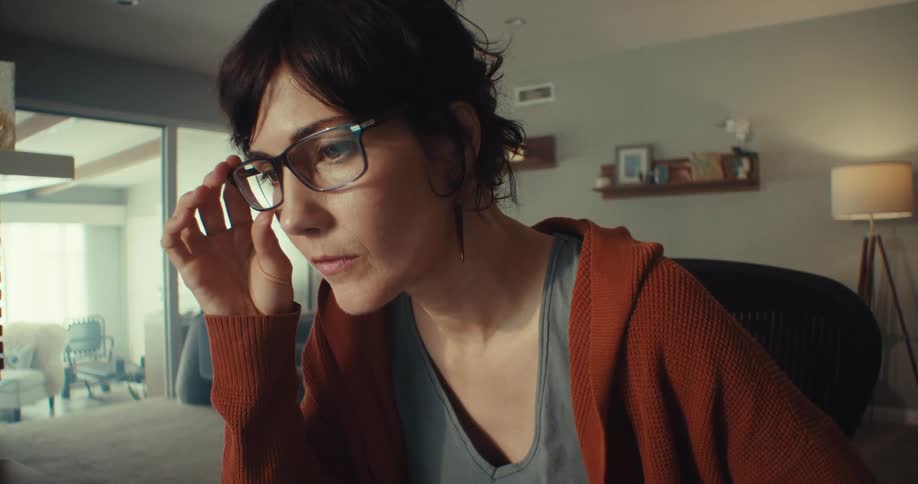 A woman wearing glasses sits in front of a computer screen in her sitting room at midday