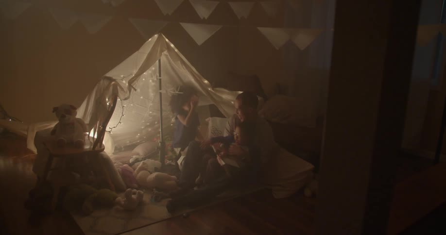 A man and children read a book under a blanket tent