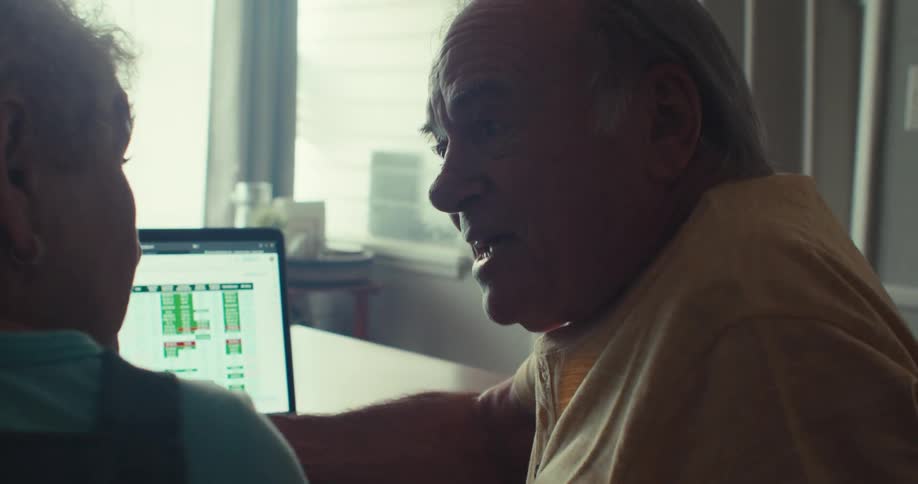 An elderly couple hugs with joy while chatting and smiling in front of a laptop