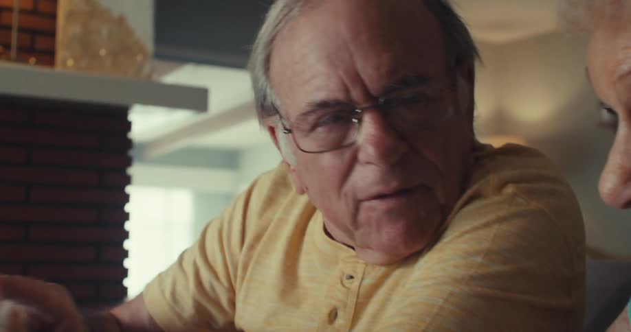 Two older adults sit indoors attentively analyzing something on a laptop together