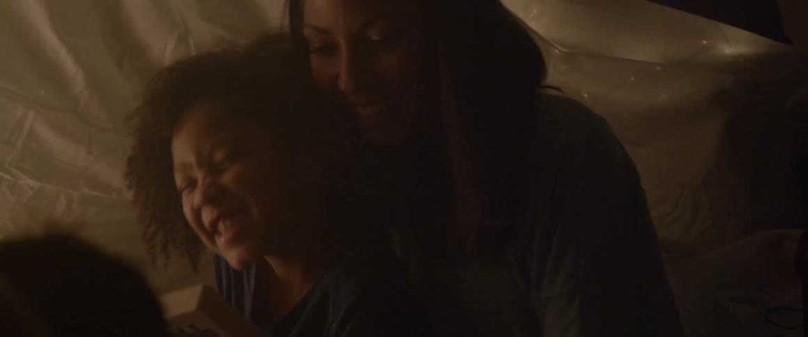 A woman and girl smile and hug inside a blanket tent