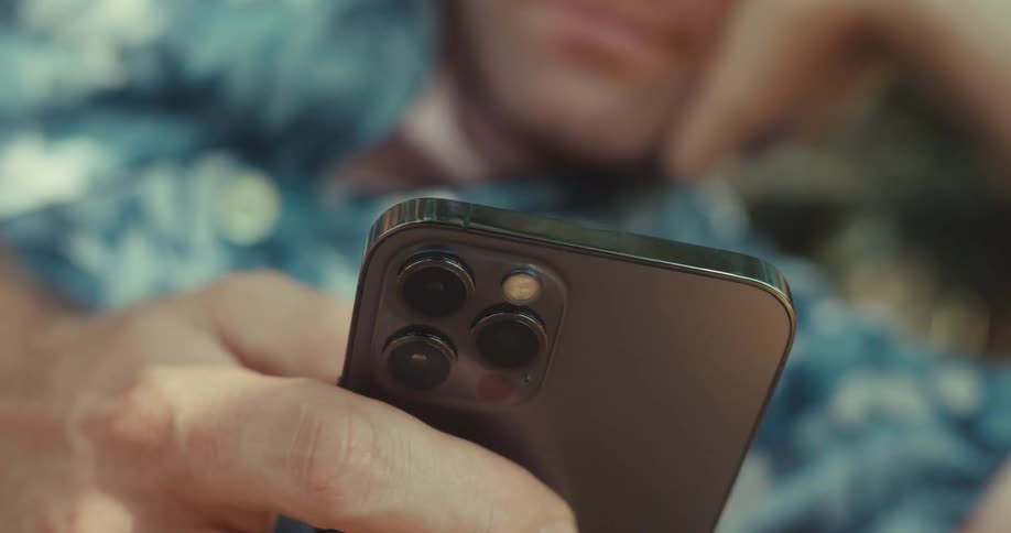 Man scrolls on his smartphone while lying on the ground outdoors during the daytime