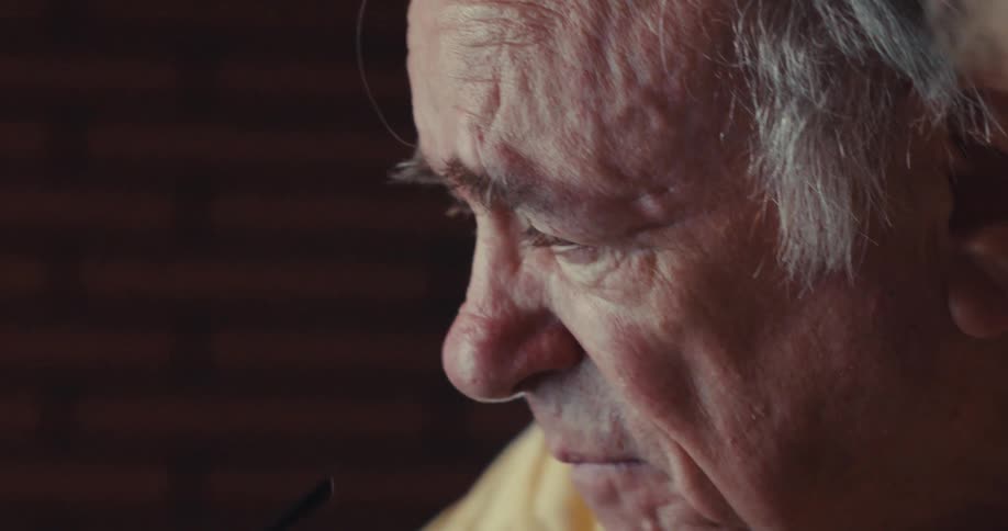 An elderly man takes off his glasses after pointing at a computer screen laughing and talking to his wife while indoors