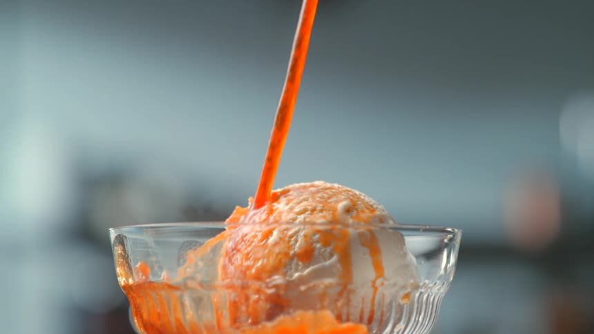 Coffee/ caramel flows over a scoop of vanilla ice cream in a glass container