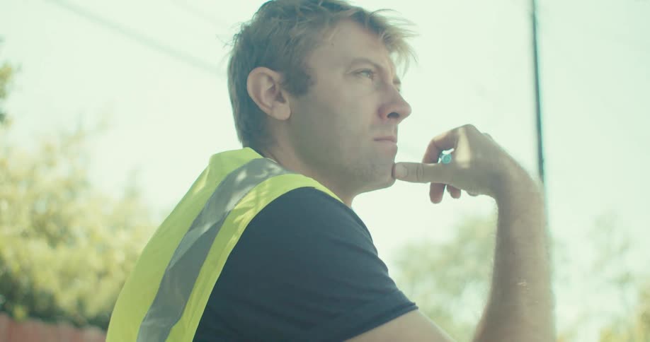Man wearing a safety vest sits outdoors at a table with a pen