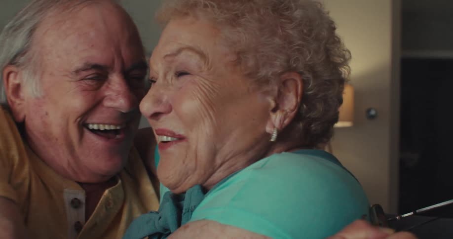An elderly couple hugs tightly while laughing with happy emotional expressions