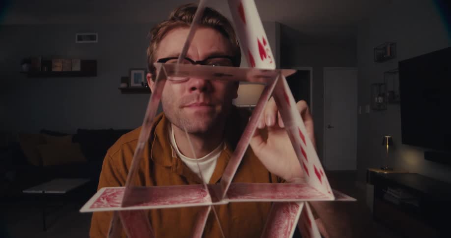 A man in a living room admiring a tower made of playing cards