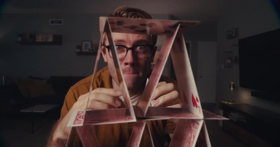 Man carefully arranges two cards on a stack of similar cards in a living room
