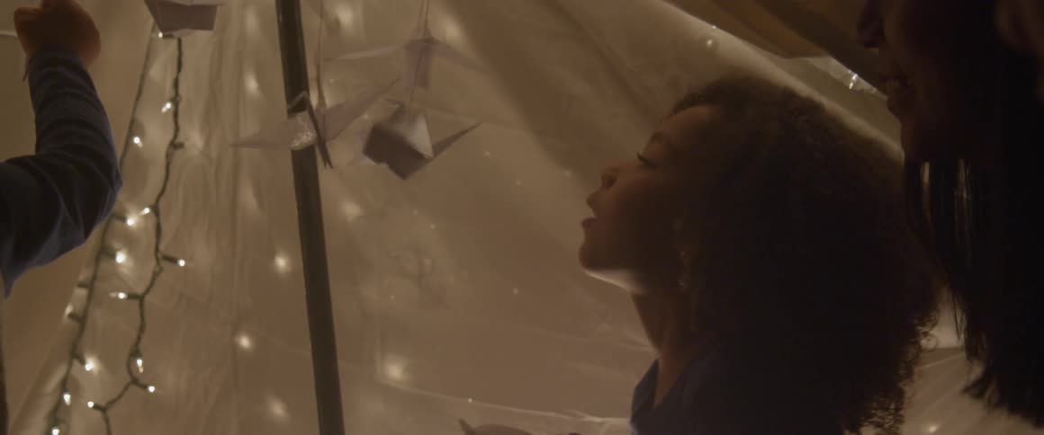 Children play with paper birds hanging inside a fort with lights