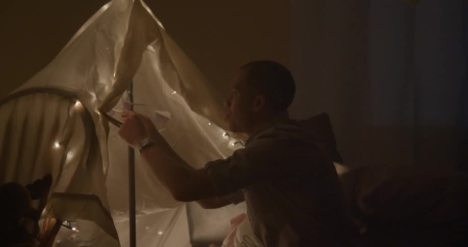 Man hangs an origami bird inside an indoor fort