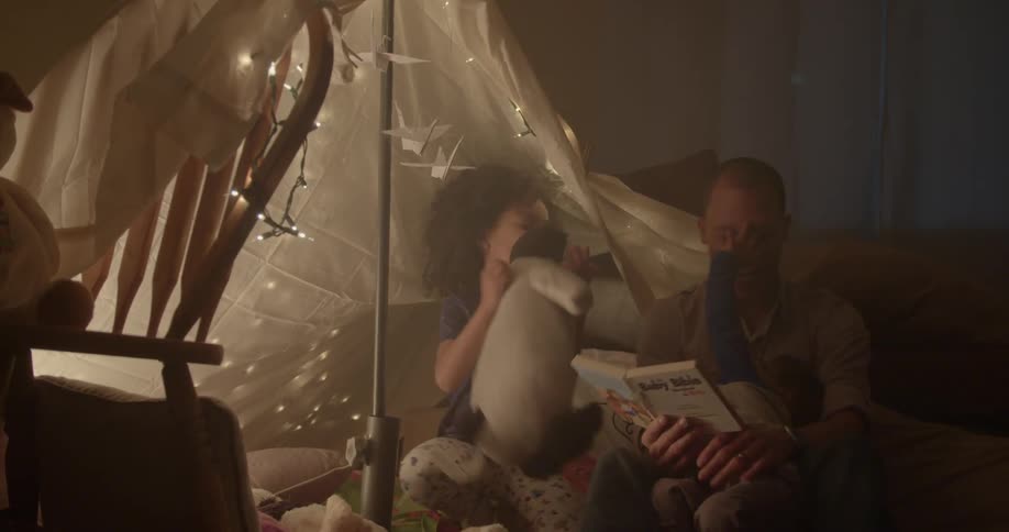 A man reads a book to his children in a blanket tent