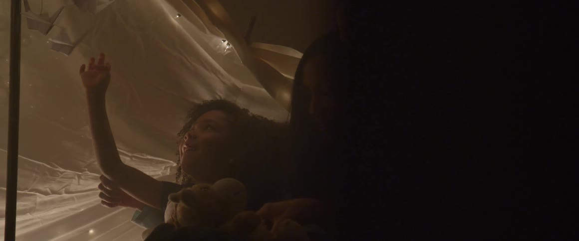 A family lays together in a blanket tent illuminated with small lights