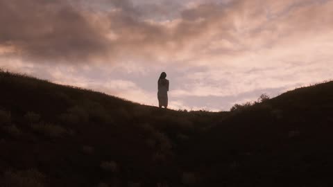 A woman walks over the hill at sunrise