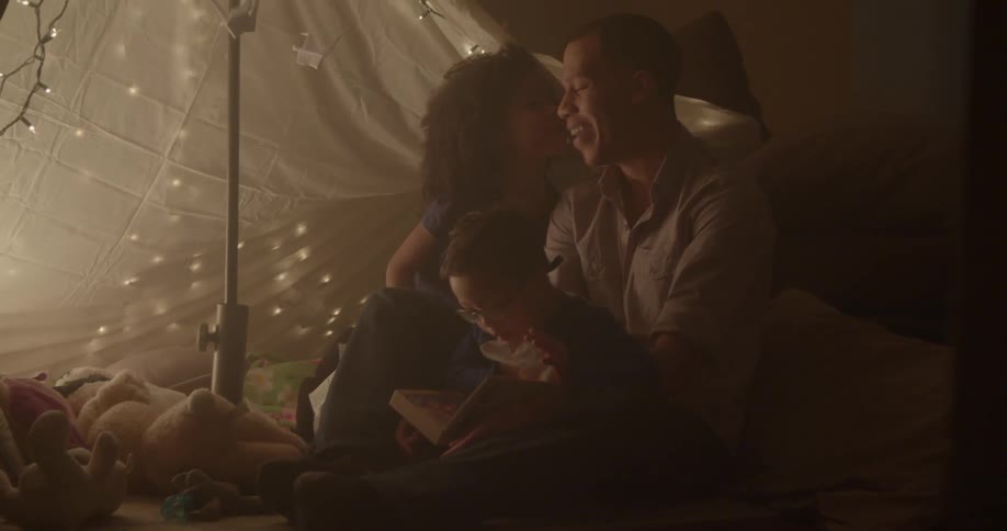 A man reads a book to his children in a blanket tent