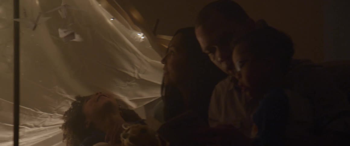 A family sits inside a blanket tent and reads a book