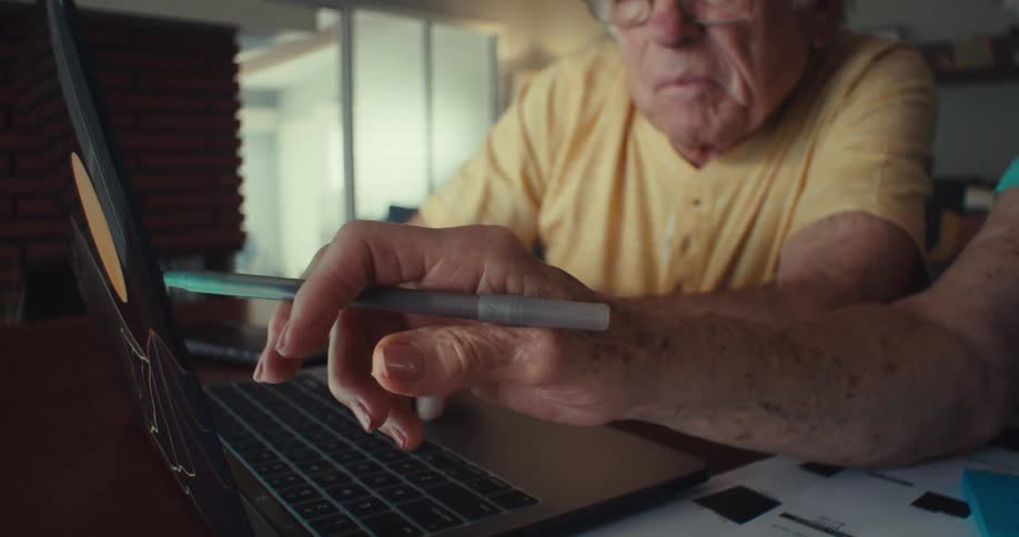 An older couple looks at a laptop screen together discussing and taking notes