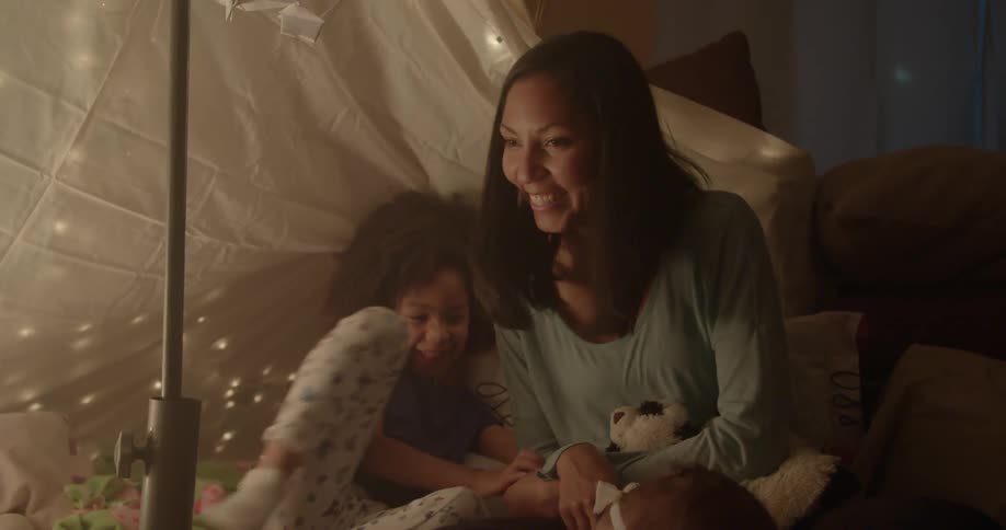 A woman plays with a young girl in a blanket tent