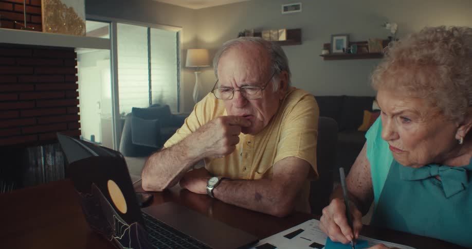 A man and woman talk and write while looking at a laptop