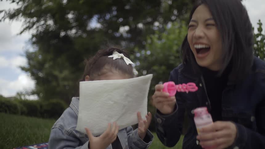 Mother playfully blows bubbles onto her daughters face during fun time at the park