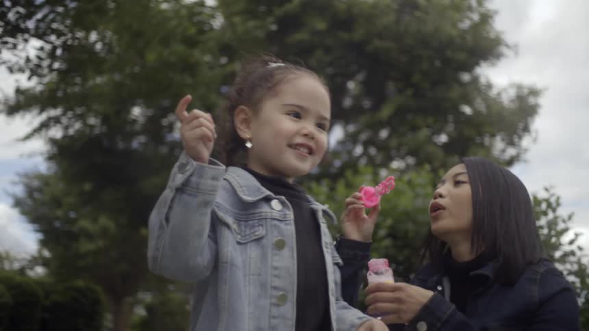 A mother blows bubbles as her daughter chases them