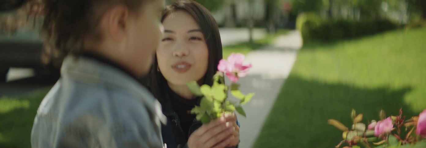 A mother and daughter enjoying gardening outdoors with the child smelling a flower