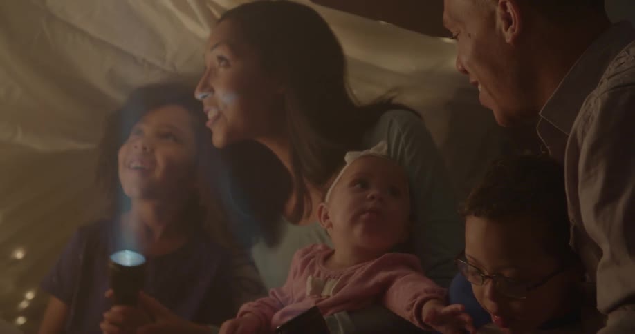 A family sits on the floor with flashlights in a blanket tent