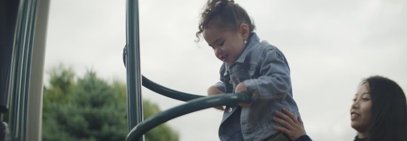 A mother helps her daughter climb on a slide