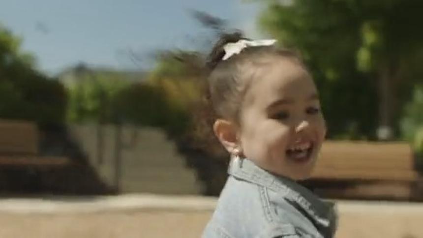 A girl child playfully runs to meet an adult woman sitting in a playground during the day