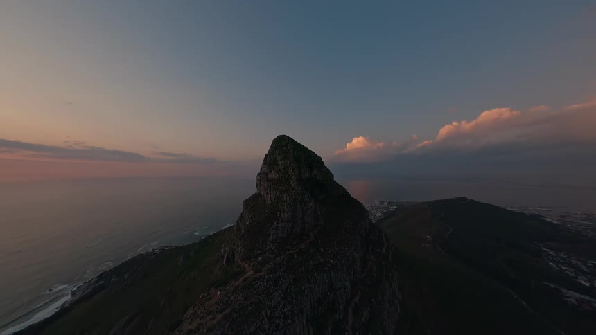 Aerial of a steep mountain peak overlooking the ocean at sunset