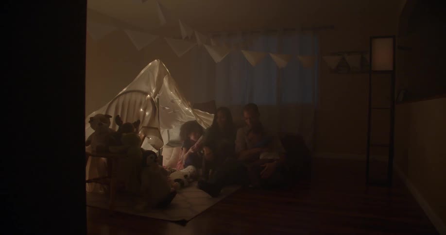 Several people including children running into a room to sit next to a man and woman that are already sitting on the floor