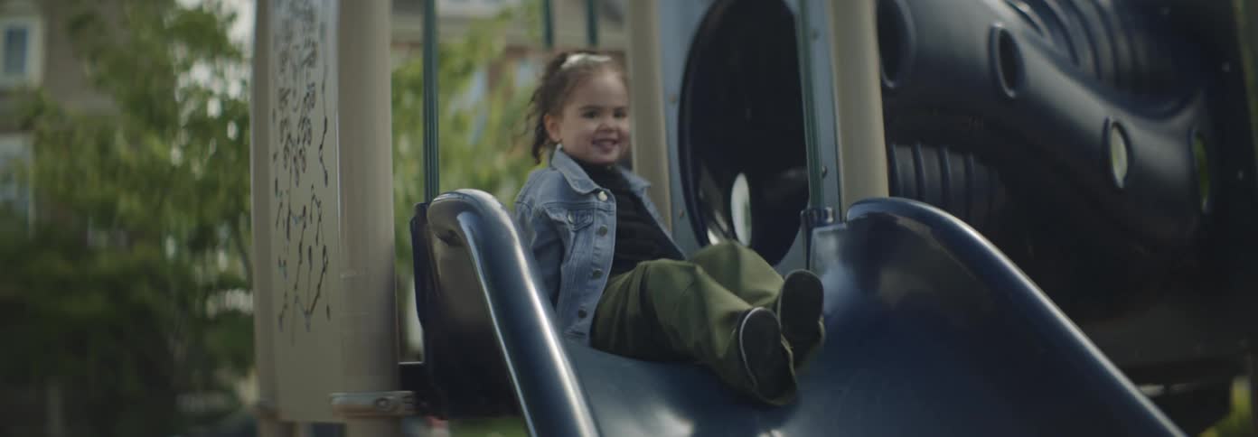 A girl playfully goes down a slide in a playground during the day