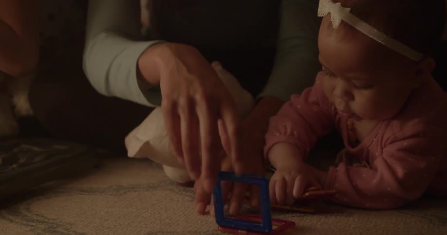 Person playing with an infant that is lying on her belly on the floor