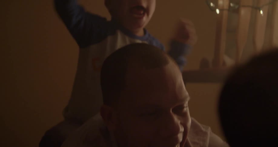 A man laughs as a child sits and plays on his back