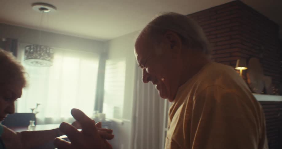 An elderly couple holds hands and dances joyfully indoors with big smiles