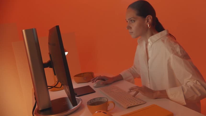 A woman wearing a white shirt is working on the computer in an orange room