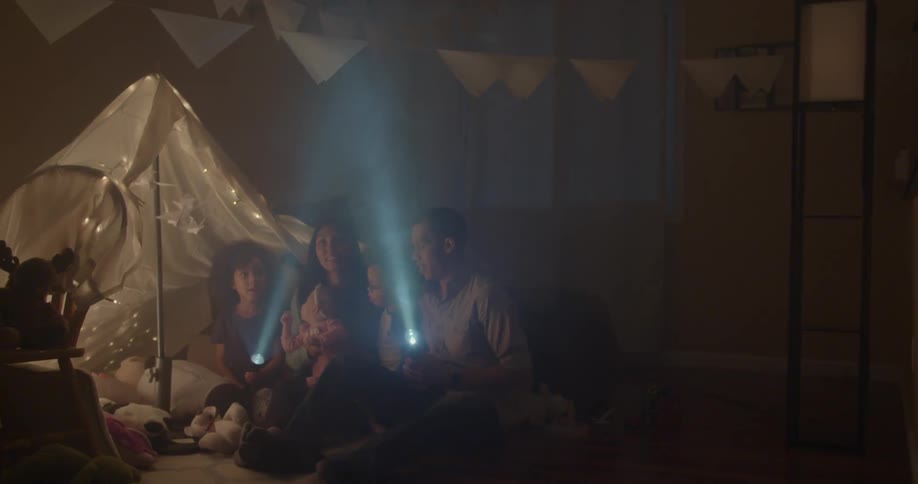 Group of people including children shining two flashlights indoors at some decorations hanging from some lines