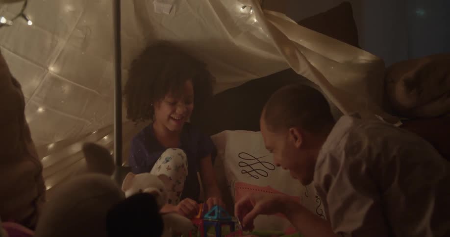 Man and young child playing under a homemade tent indoors