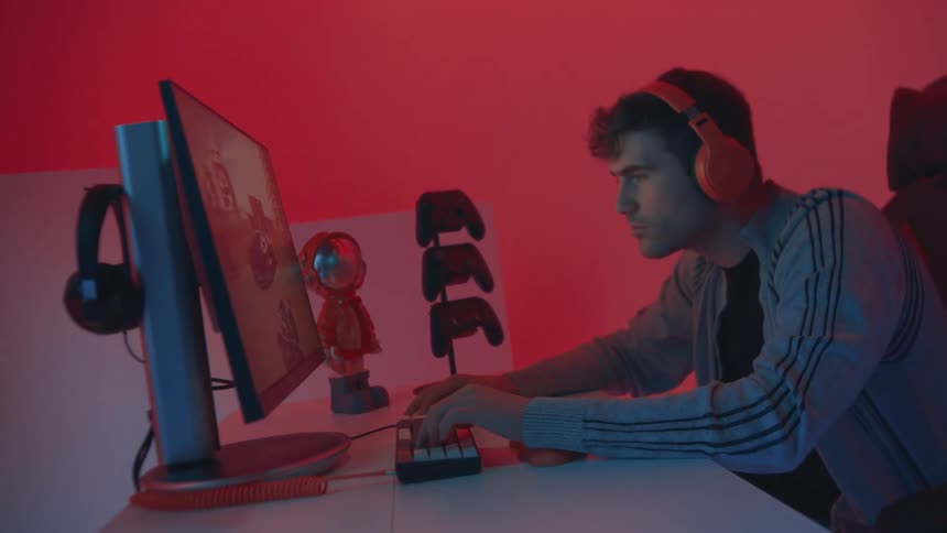 Man plays video games on a desktop computer setup in a red lit room
