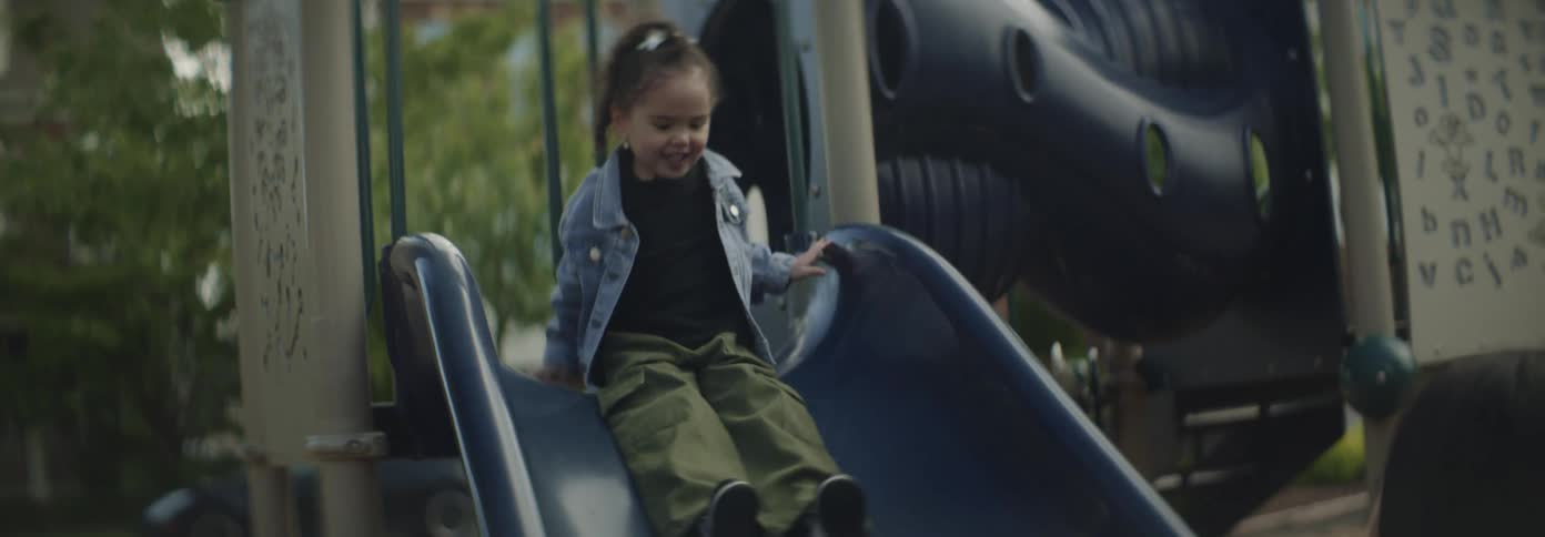 Woman catches a girl after she playfully slides down in a playground