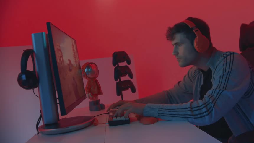 A young man intensely plays a video game on a pc in a neonlit gaming setup