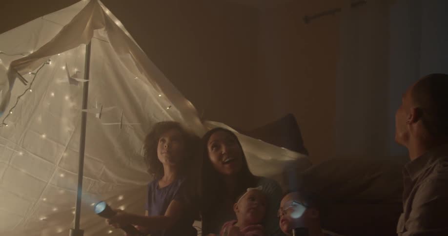 A family sits on the floor with flashlights in a blanket tent