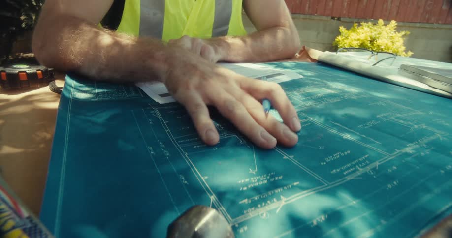 A construction worker sketches a plan on a chart while kneeling on a grassy lawn