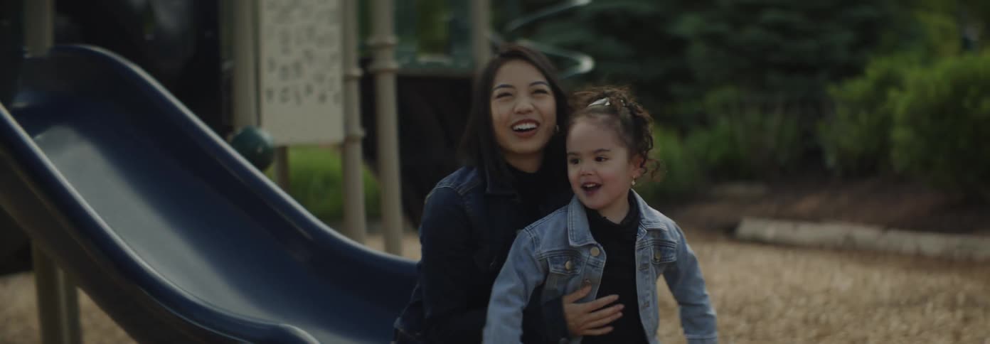 An asian mother playing with her daughter in a childrens park sliding down the slide with excitement at midday