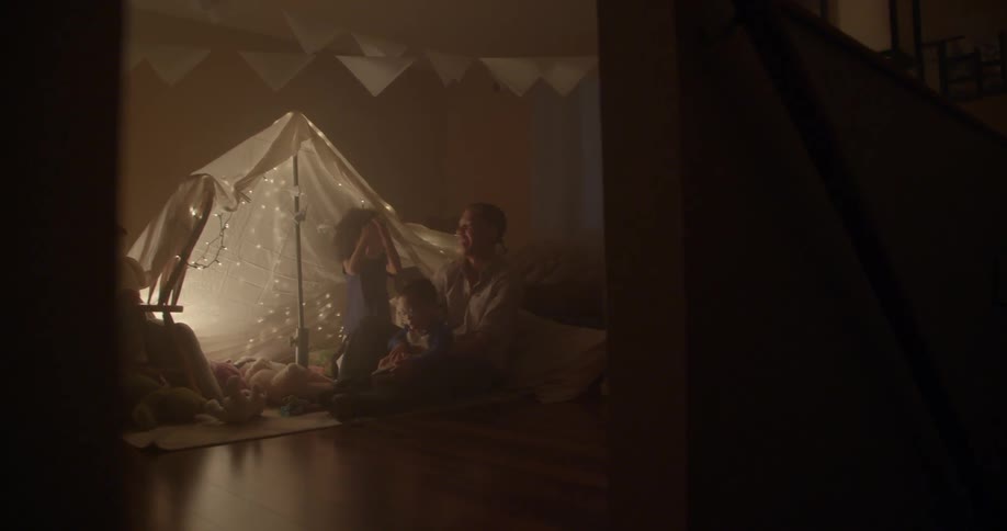 Man talking to infant children while sitting on the floor next to a tent set up indoors