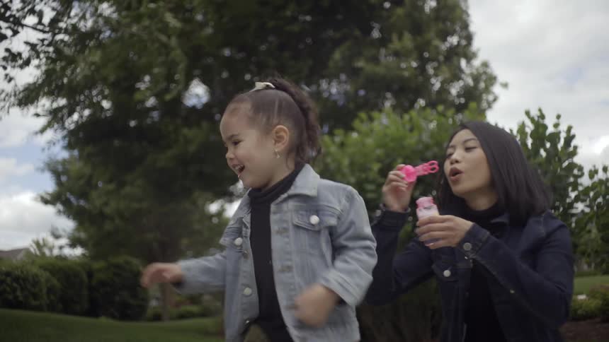A woman blowing soap bubbles and a child running to try to catch them
