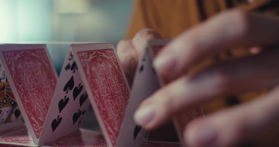 A man with glasses intently builds a house of cards carefully placing each card with a slight smile on his face