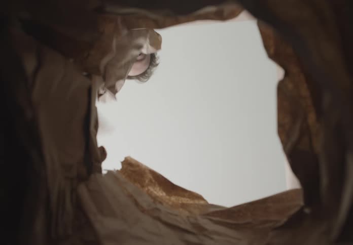 Man wraps a small white box with brown paper and places it inside a paper bag