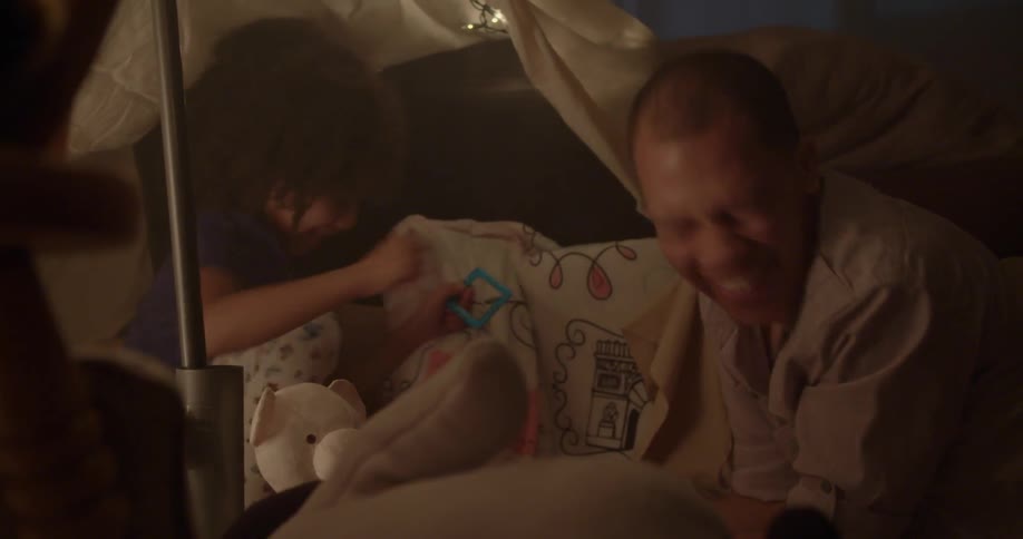 A man and child tickle each other and laugh under a blanket tent