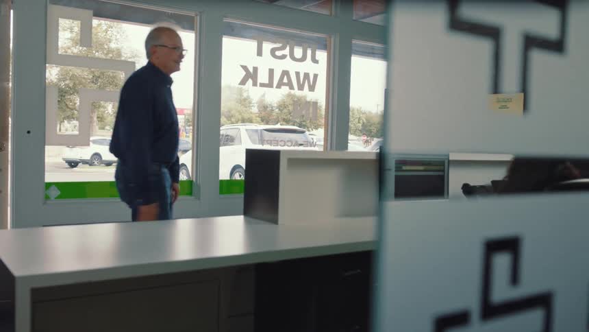 An older man speaks to a receptionist at a modern office front desk