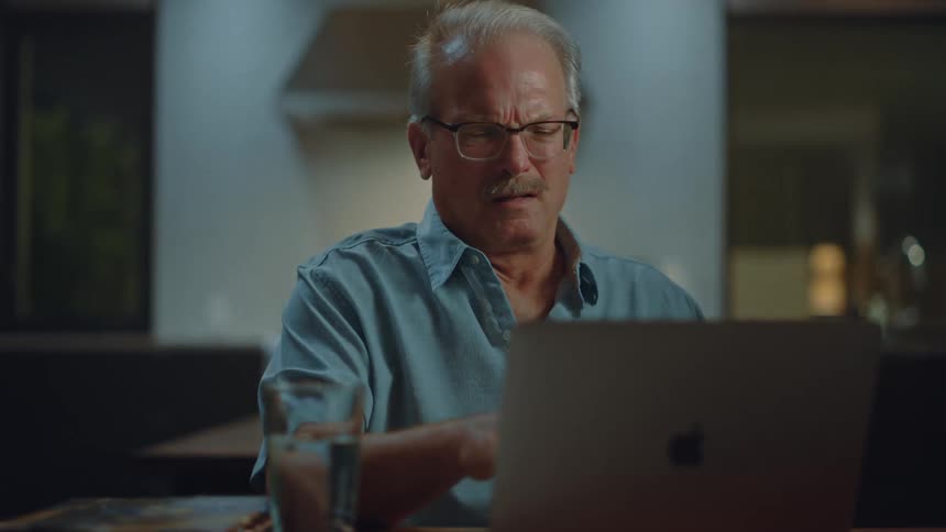 A man typing on his laptop holds his stomach in pain